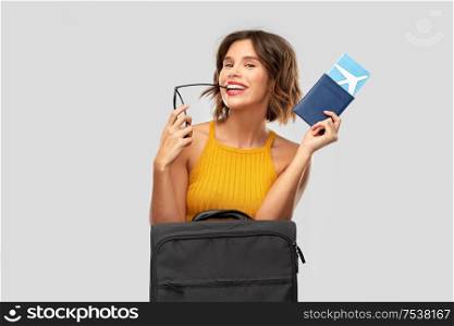 travel, tourism and vacation concept - happy laughing young woman in mustard yellow top with air ticket, carry-on bag and passport over grey background. happy young woman with air ticket and travel bag