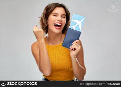 travel, tourism and vacation concept - happy laughing young woman in mustard yellow top with air ticket and passport making fist pump gesture over grey background. happy young woman with air ticket and passport