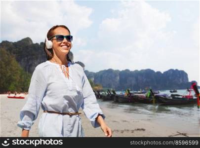 travel, tourism and vacation concept - happy smiling woman with headphones walking over tropical beach background in french polynesia. woman with headphones walking along tropical beach
