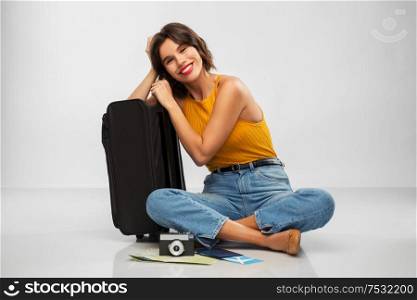 travel, tourism and vacation concept - happy smiling young woman in mustard yellow top with air ticket, camera, map and carry-on bag over grey background. woman with travel bag, air ticket, map and camera