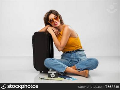 travel, tourism and vacation concept - happy smiling young woman in mustard yellow top with air ticket, camera, map and carry-on bag over grey background. woman with travel bag, air ticket, map and camera