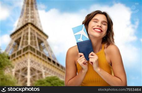 travel, tourism and vacation concept - happy smiling young woman in yellow top with air ticket and passport over eiffel tower in paris, france background. happy woman with air ticket over eiffel tower