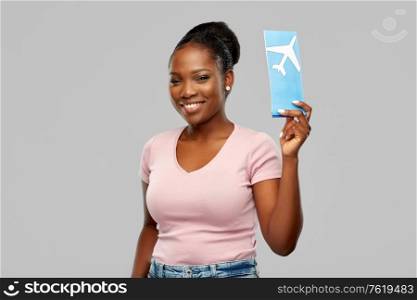 travel, tourism and vacation concept - happy young african american woman with air ticket over grey background. happy african american woman with air ticket