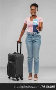 travel, tourism and vacation concept - happy young african american woman with air ticket, passport and carry-on bag over grey background. happy young woman with air ticket and travel bag