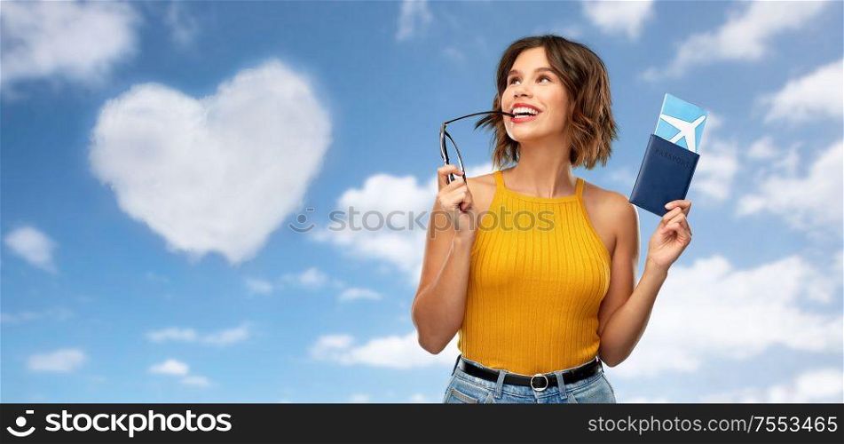 travel, tourism and vacation concept - happy young woman in mustard yellow top with air ticket and passport dreaming over blue sky and clouds background. happy young woman with air ticket and passport