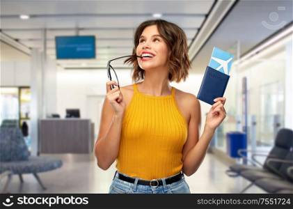 travel, tourism and vacation concept - happy young woman in yellow top with air ticket and passport dreaming over airport lounge background. happy young woman with air ticket at airport