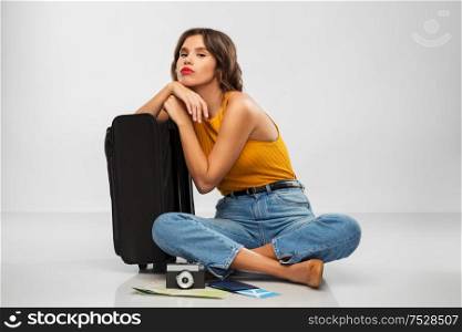 travel, tourism and vacation concept - sad young woman in mustard yellow top with air ticket, camera, map and carry-on bag over grey background. woman with travel bag, air ticket, map and camera
