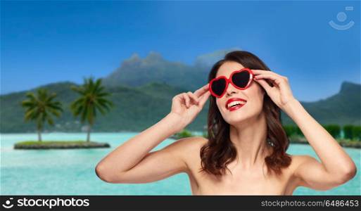 travel, tourism and valentines day concept - happy smiling young woman with red lipstick and heart shaped sunglasses over bora bora resort beach background in french polynesia. woman with sunglasses over bora bora beach. woman with sunglasses over bora bora beach