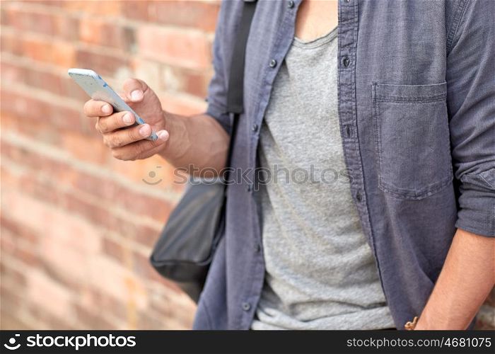 travel, tourism, communication, technology and people concept - close up of man with bag texting on smartphone on city street