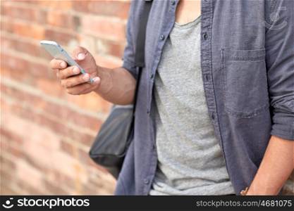 travel, tourism, communication, technology and people concept - close up of man with bag texting on smartphone on city street