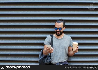 travel, tourism, communication, technology and people concept - man with backpack and coffee cup texting on smartphone on city street