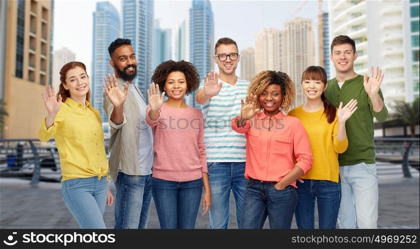 travel, tourism, diversity and people concept - international group of happy smiling men and women waving hand over dubai city street background. international group of people waving hand in city