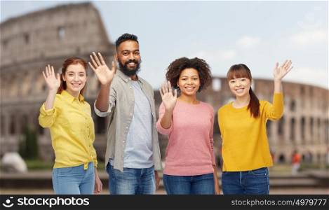 travel, tourism, diversity and people concept - international group of happy smiling men and women waving hands over coliseum background. international group of happy people waving hands