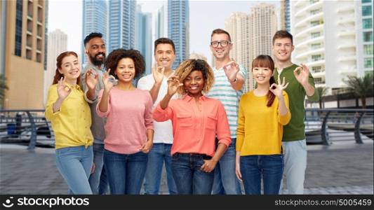travel, tourism, diversity, ethnicity and people concept - international group of happy smiling men and women showing ok hand sign over dubai city street background. international group of people showing ok in city