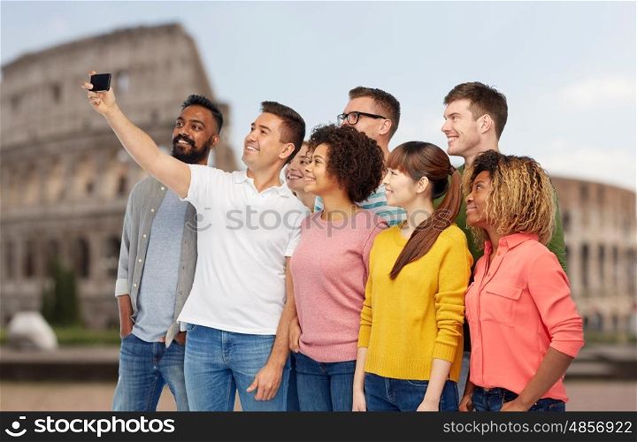 travel, tourism, diversity, technology and people concept - international group of happy smiling men and women taking selfie by smartphone over coliseum background