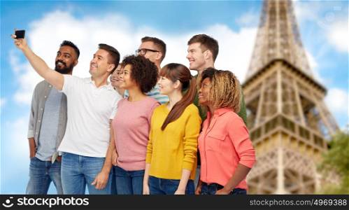 travel, tourism, diversity, technology and people concept - international group of happy smiling men and women taking selfie by smartphone over eiffel tower background. group of people taking selfie by smartphone