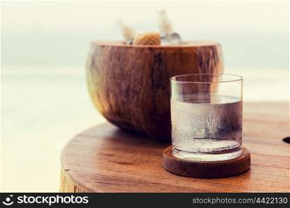 travel, tourism, drinks and refreshment concept - glass of cold water an moisturizing stuff on table at beach