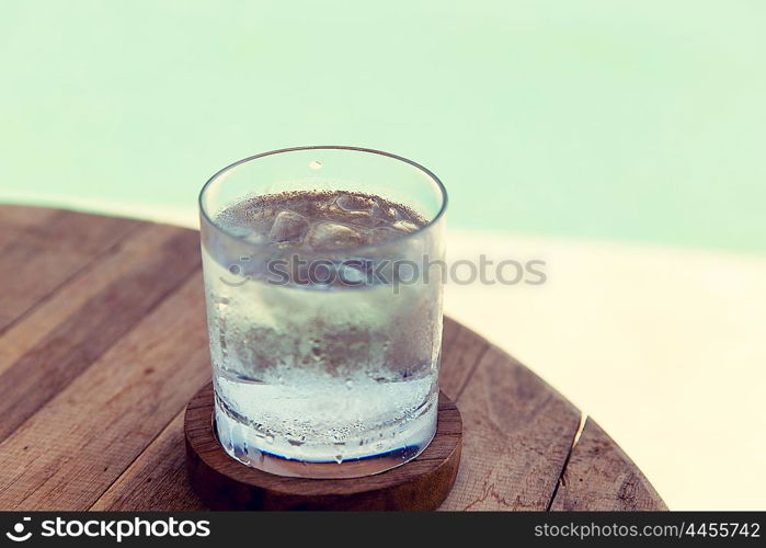 travel, tourism, drinks and refreshment concept - glass of cold water with ice cubes on table at beach