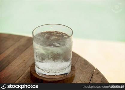 travel, tourism, drinks and refreshment concept - glass of cold water with ice cubes on table at beach