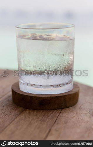 travel, tourism, drinks and refreshment concept - glass of cold water with ice cubes on table at beach