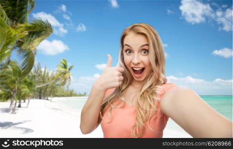 travel, tourism, emotions, expressions and people concept - happy smiling young woman taking selfie and showing thumbs up over exotic tropical beach with palm trees background