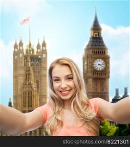 travel, tourism, emotions, expressions and people concept - happy smiling young woman taking selfie over big ben london and city background