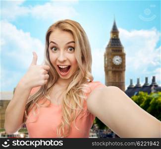 travel, tourism, emotions, expressions and people concept - happy smiling young woman taking selfie and showing thumbs up over big ben london and city background