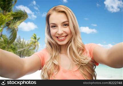 travel, tourism, emotions, expressions and people concept - happy smiling young woman taking selfie over exotic tropical beach with palm trees background