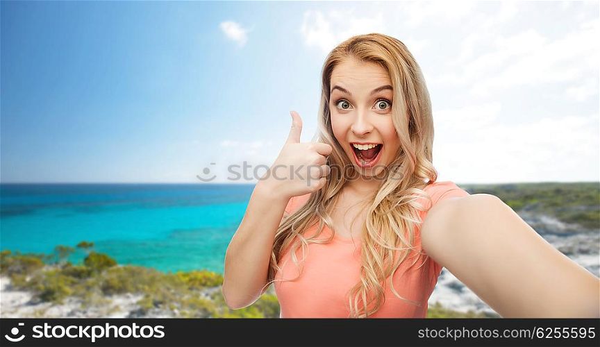 travel, tourism, emotions, expressions and people concept - happy smiling young woman taking selfie and showing thumbs up over exotic tropical beach background