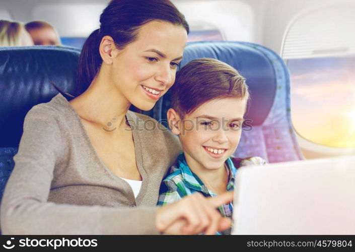 travel, tourism, family and technology concept - happy mother and son with tablet pc computer sitting in plane over porthole background. happy family with tablet pc sitting in plane. happy family with tablet pc sitting in plane