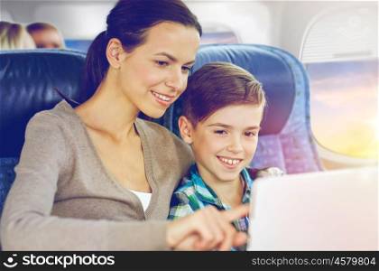 travel, tourism, family and technology concept - happy mother and son with tablet pc computer sitting in plane over porthole background. happy family with tablet pc sitting in plane. happy family with tablet pc sitting in plane