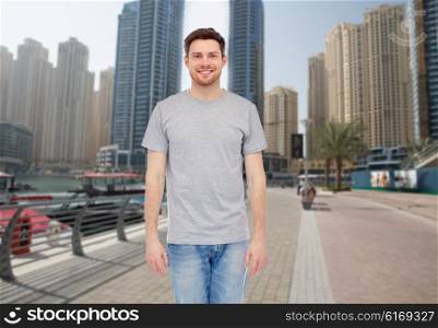 travel, tourism, fashion and people concept - smiling young man in gray t-shirt and jeans over dubai city street background