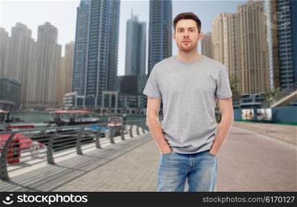 travel, tourism, fashion and people concept - young man in gray t-shirt and jeans over dubai city street background