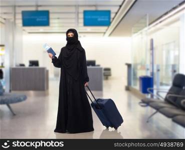travel, tourism, flight and people concept - muslim woman in hijab with airplane ticket, passport and carry-on bag over airport waiting room background. muslim woman with ticket, passport and travel bag