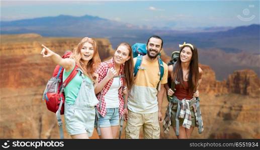 travel, tourism, hike and adventure concept - group of smiling friends with backpacks pointing finger to something over grand canyon national park background. group of friends with backpacks at grand canyon. group of friends with backpacks at grand canyon