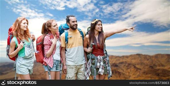 travel, tourism, hike and adventure concept - group of smiling friends with backpacks pointing finger to something over grand canyon national park hills background. group of friends with backpacks over mountains
