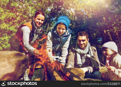 travel, tourism, hike and camping concept - happy family roasting marshmallow over campfire. happy family roasting marshmallow over campfire