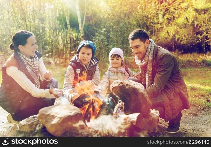 travel, tourism, hike and camping concept - happy family roasting marshmallow over campfire. happy family roasting marshmallow over campfire