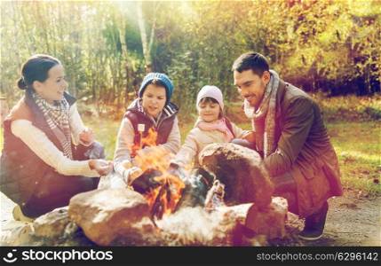 travel, tourism, hike and camping concept - happy family roasting marshmallow over campfire. happy family roasting marshmallow over campfire