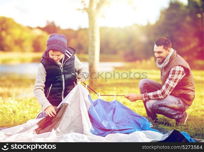 travel, tourism, hike and family concept - happy father and son setting up tent outdoors. happy father and son setting up tent outdoors