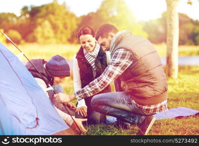 travel, tourism, hike and family concept - happy mother, father and son setting up tent outdoors. happy family setting up tent outdoors