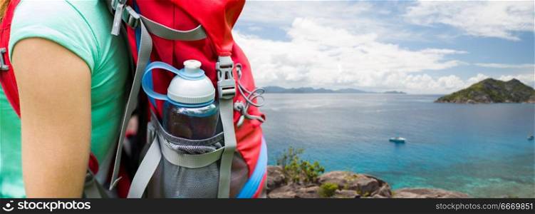 travel, tourism, hike and people concept - close up of woman with water bottle in backpack pocket over background of seychelles island in indian ocean. close up of woman with water bottle in backpack. close up of woman with water bottle in backpack