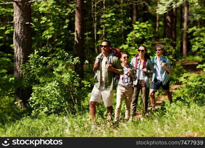 travel, tourism, hike and people concept - group of friends walking with backpacks in forest. group of friends with backpacks hiking in forest