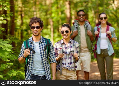 travel, tourism, hike and people concept - group of friends walking with backpacks in forest. group of friends with backpacks hiking in forest