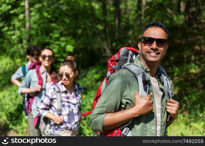 travel, tourism, hike and people concept - group of friends walking with backpacks in forest. group of friends with backpacks hiking in forest