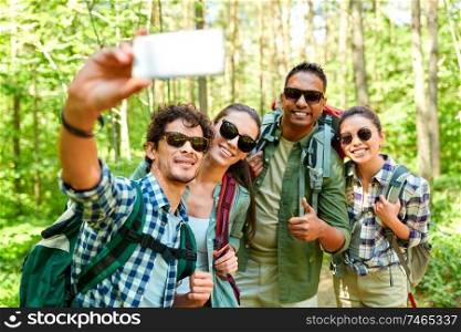 travel, tourism, hike and people concept - group of friends with backpacks taking selfie by smartphone in forest. friends with backpacks hiking and taking selfie