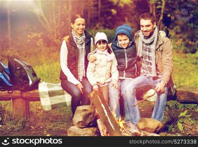 travel, tourism, hike and people concept - happy family sitting on bench at camp fire in woods. happy family sitting on bench at camp fire