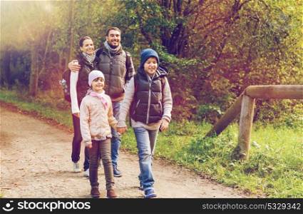 travel, tourism, hike and people concept - happy family walking with backpacks along road in woods. happy family with backpacks hiking in woods