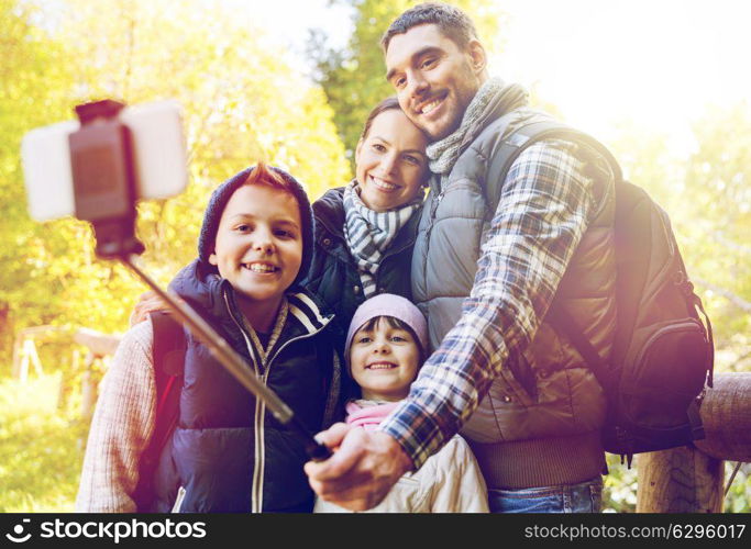 travel, tourism, hike and people concept - happy family with backpacks hiking and taking picture by smartphone on selfie stick. family with backpacks taking selfie and hiking