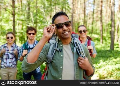 travel, tourism, hike and people concept - man in sunglasses and group of friends with backpacks in forest. friends with backpacks on hike in forest